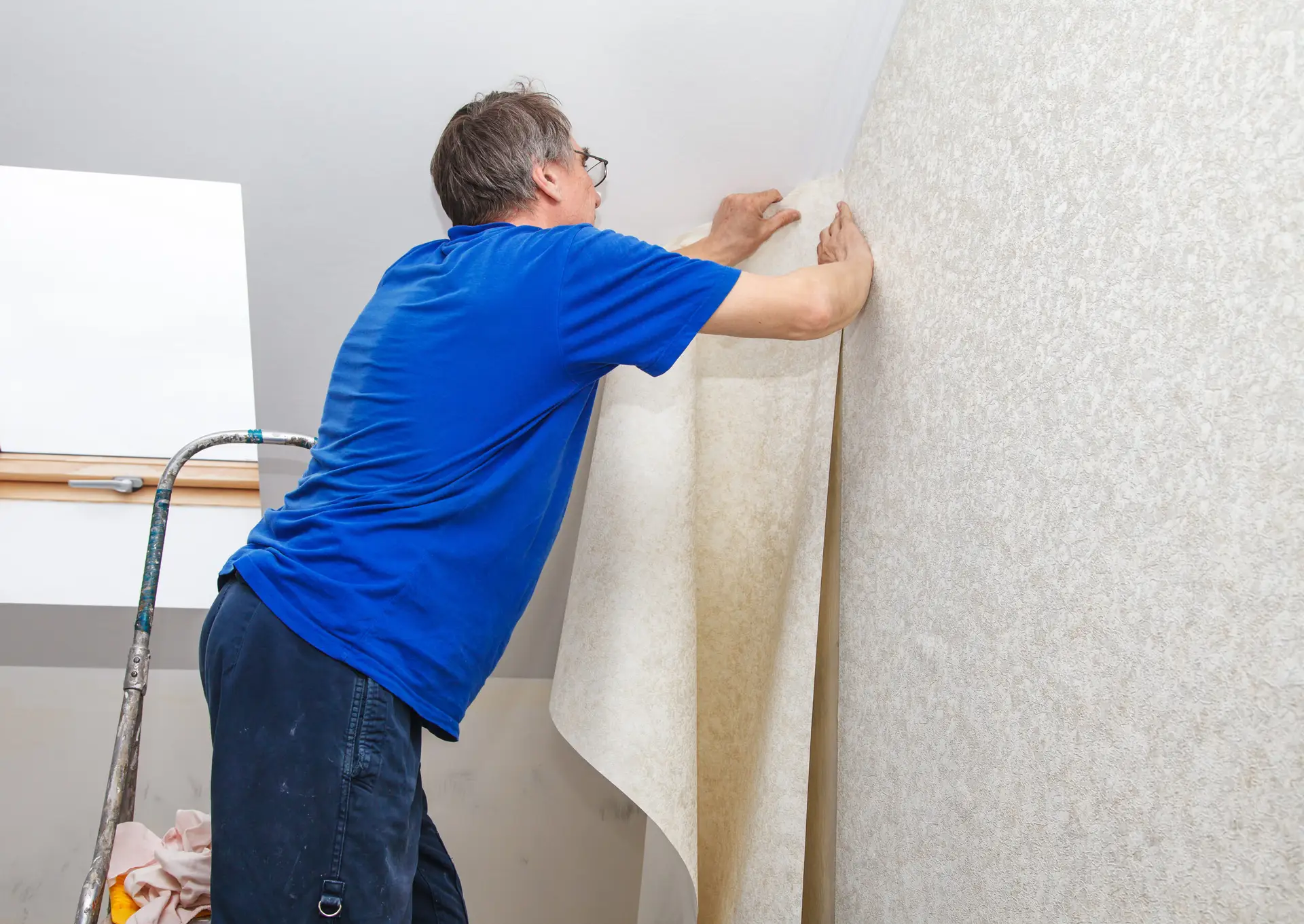 elderly worker smoothing wallpaper in his house